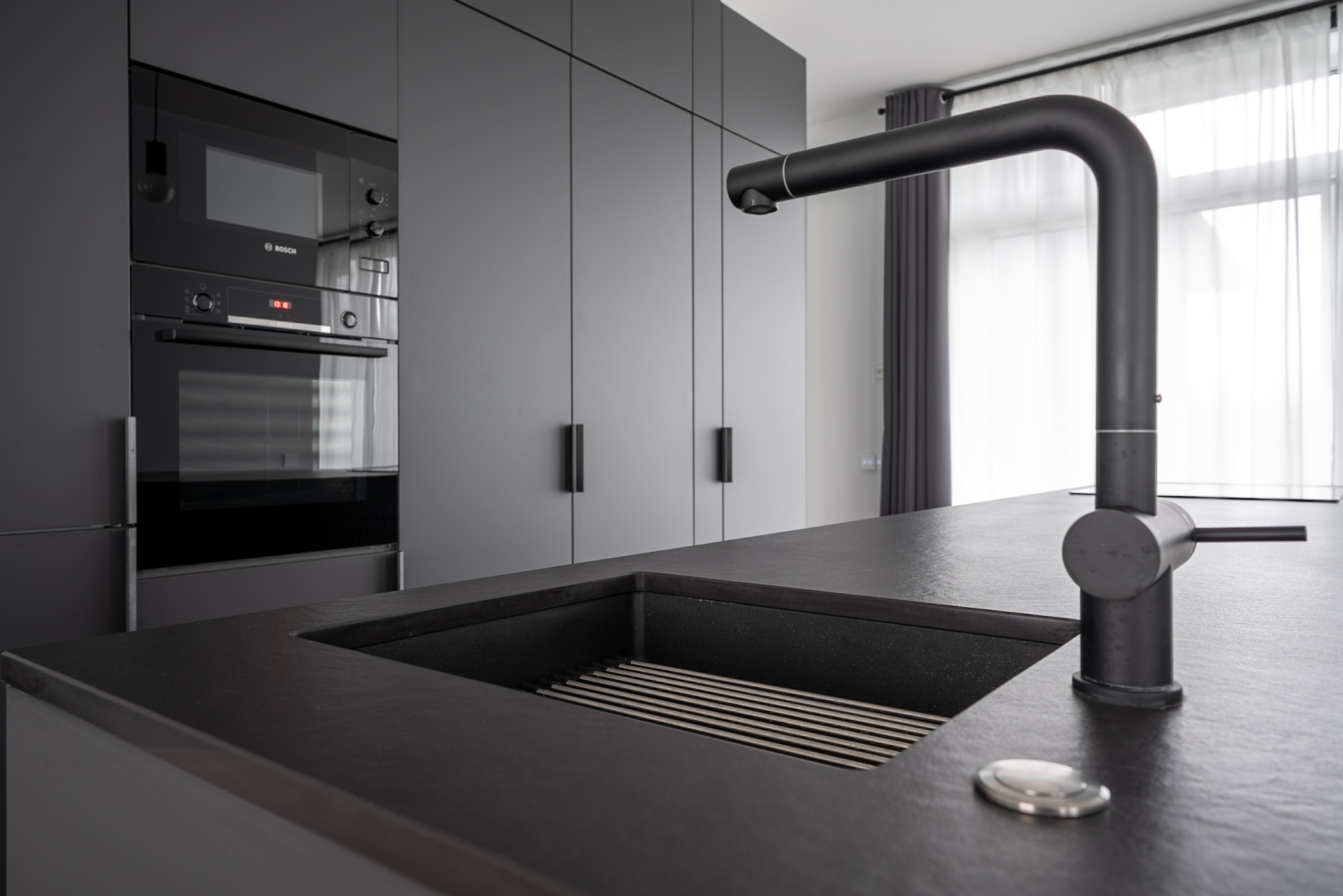 Кухонная мебель темно-серого цвета с матовыми фасадами, каменной поверхностью и интегрированной мойкой