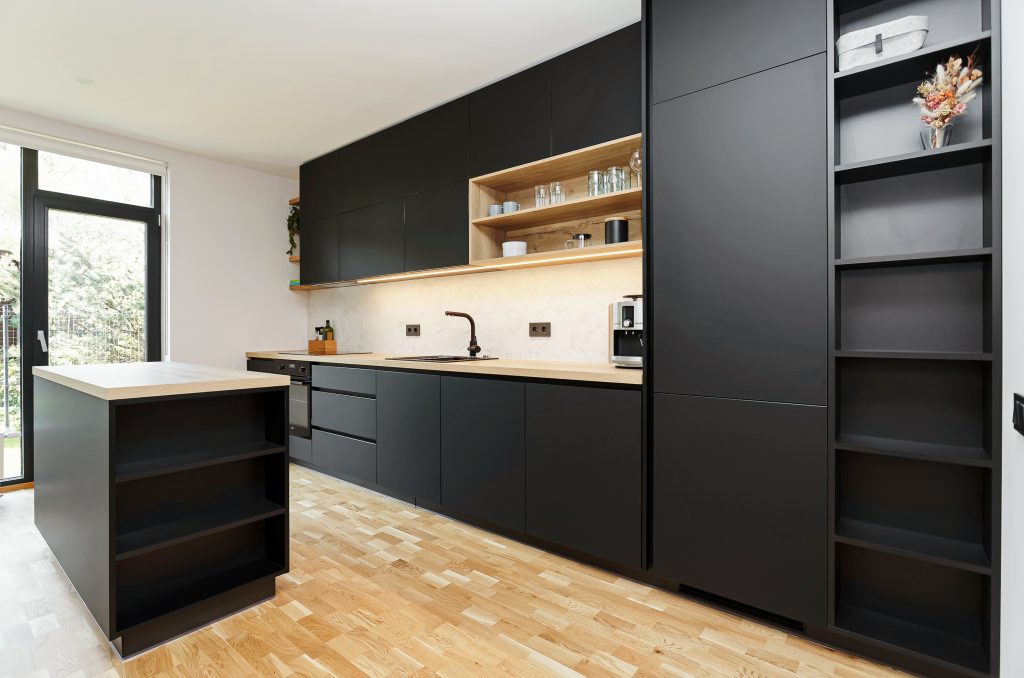 Sāna skats uz drosmīgu un melnu virtuves dizainu Čiekurkalnā, Rīgā, kas izceļas kā dinamisks akcents mierīgajā dzīvokļa interjerā